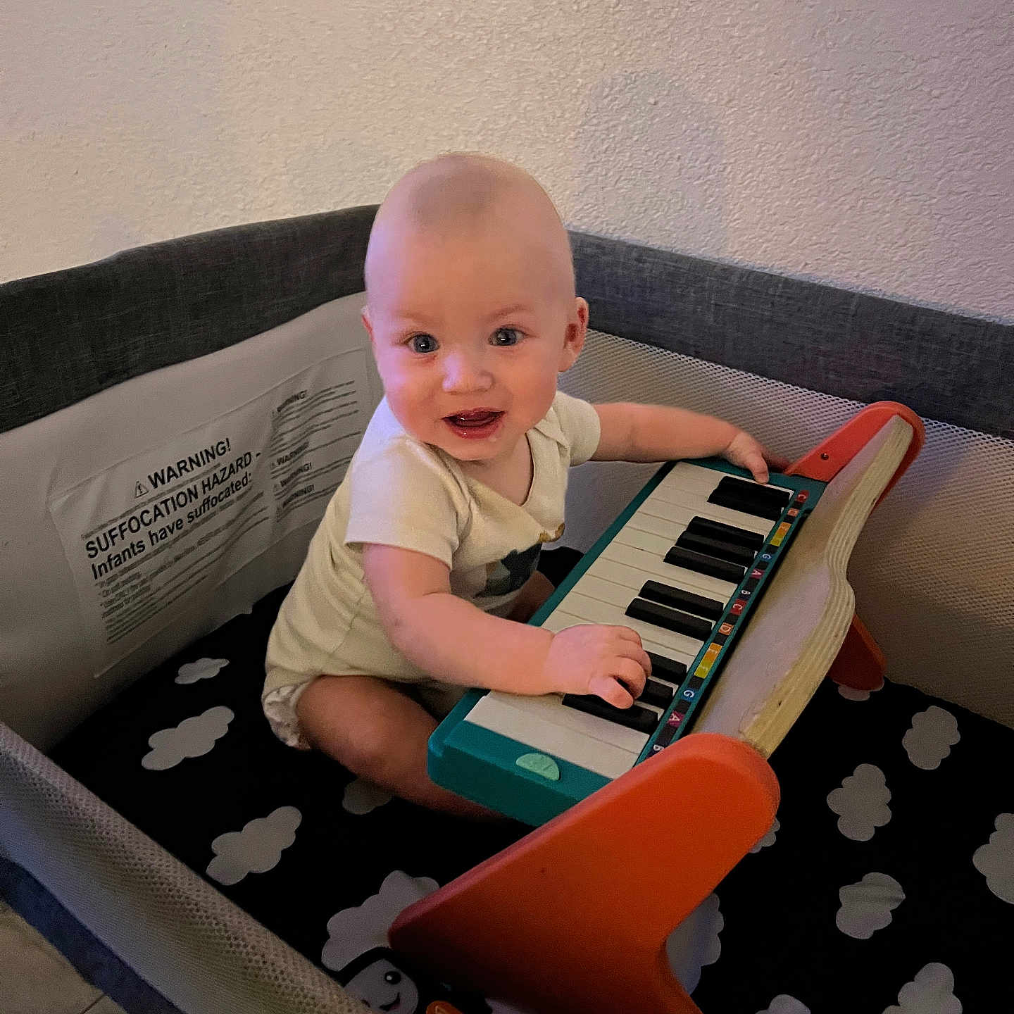 Mikey joined the competition — help win amazing prizes! baby, child, colorful, cute, face, floor, happy, indoor, infant, musical_instrument, person, piano, plastic, play, playpen, short_sleeves, sitting, smiling, toy, wall