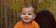 Liam is registered to the contest to win money with this photo: baby, child, smiling, orange_shirt, person, forest, trees, autumn, outdoor, nature, portrait, head, face, happy, young, holding, hair, background, season, cute