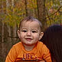 baby, child, smiling, orange_shirt, person, forest, trees, autumn, outdoor, nature, portrait, head, face, happy, young, holding, hair, background, season, cute