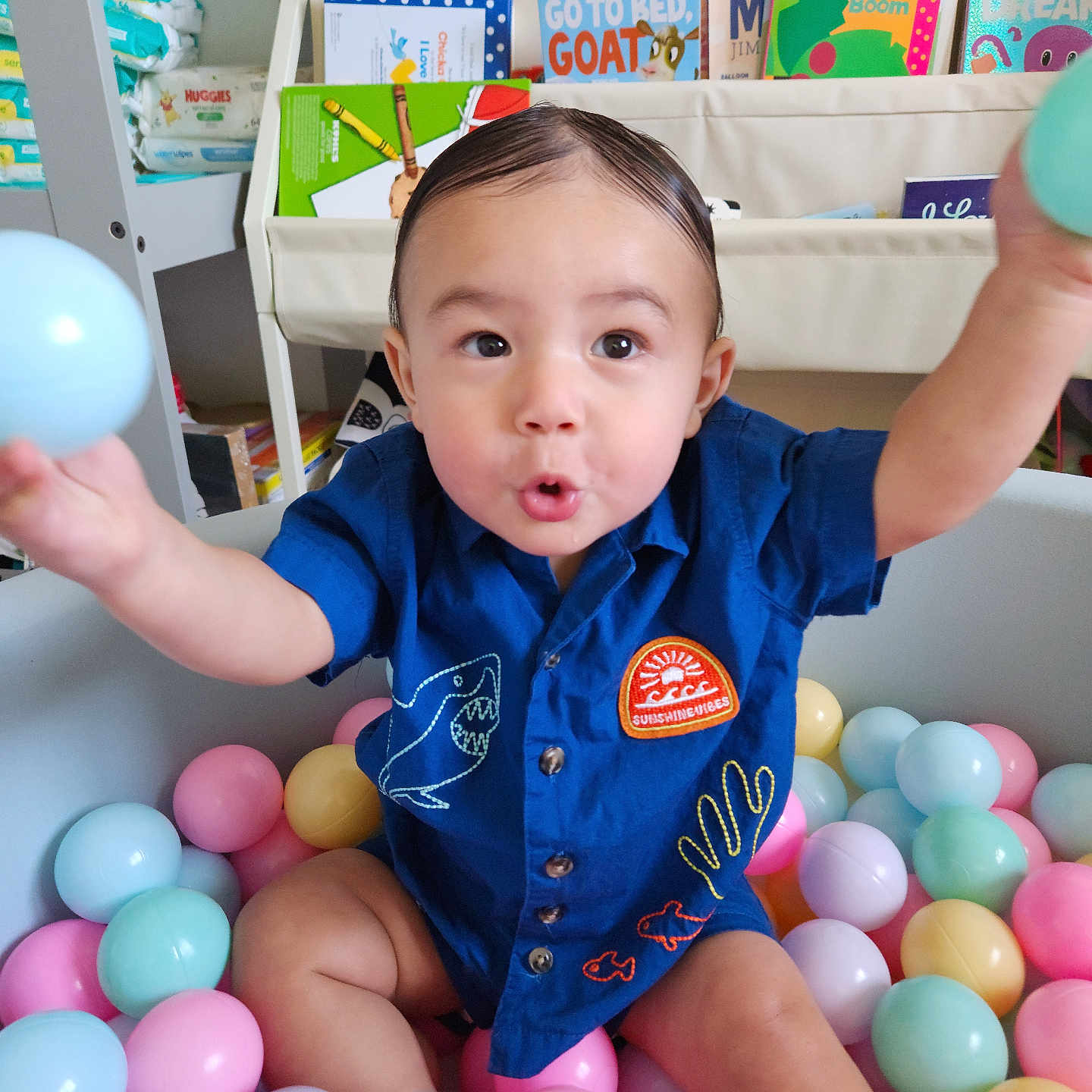 Ace is registered to the contest to win money with this photo: toddler, child, ball_pit, colorful_balls, blue_shirt, embroidery, playful_expression, indoor, bookshelf, children_books, baby_supplies, diapers, toy, happy, reaching_out, playroom, cute, portrait, person, smiling
