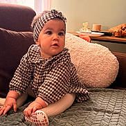 Hailey a rejoint le concours — aidez-le/la à gagner de superbes lots ! baby, child, indoor, couch, blanket, headband, checkered_clothing, sitting, cushion, table, cake, birthday_candle, footwear, hand, face, expression, soft_lighting, home, curly_hair, cozy