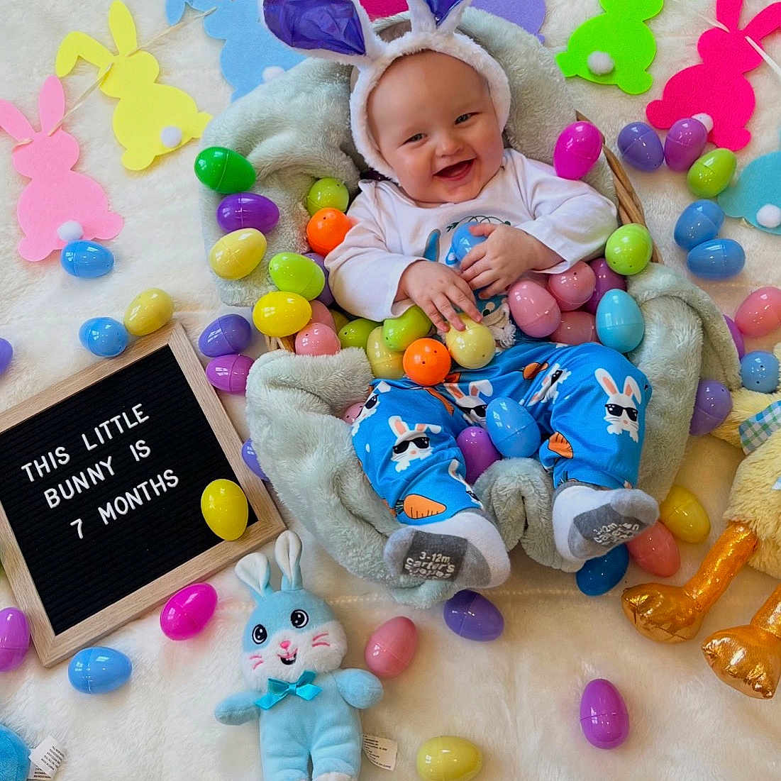 Joseph joined the competition — help win amazing prizes! baby, bunny_ears, colorful_eggs, easter_theme, plush_toy, blanket, smiling, infant, cute, playful, decorations, soft_texture, blue_pajamas, socks, happy, indoors, celebration, festive, child, portrait