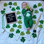 Joseph joined the competition — help win amazing prizes! baby, infant, pacifier, green_outfit, shamrock, glitter, st_patricks_day, decorations, letter_board, blanket, holiday, festive, cute, lying_down, celebration, child, holding_object, smiling, indoors, portrait