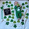 baby, infant, pacifier, green_outfit, shamrock, glitter, st_patricks_day, decorations, letter_board, blanket, holiday, festive, cute, lying_down, celebration, child, holding_object, smiling, indoors, portrait