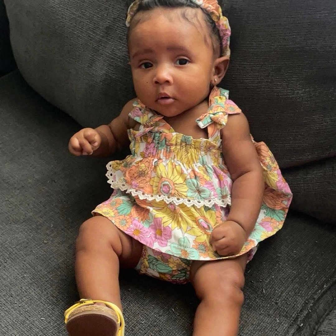 Dyomni is registered to the contest to win money with this photo: baby, child, colorful, comfortable, couch, curious, cute, dress, fashion, floral, footwear, girl, headband, indoors, infant, person, portrait, sandals, sitting, young