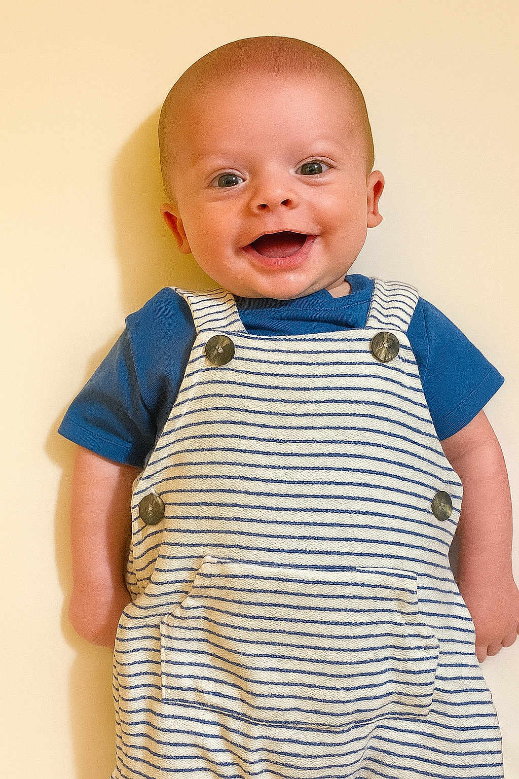 Jace is registered to the contest to win money with this photo: baby, child, smiling, happy, portrait, overalls, blue_shirt, striped_clothing, infant, cute, face, person, standing, light_background, skin, head, eyes, mouth, joy, innocence