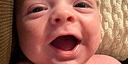 Jace is registered to the contest to win money with this photo: baby, infant, close_up, smiling, happy, face, skin, hand, blanket, texture, lying_down, cheerful, cute, child, newborn, human, portrait, emotion, soft, background