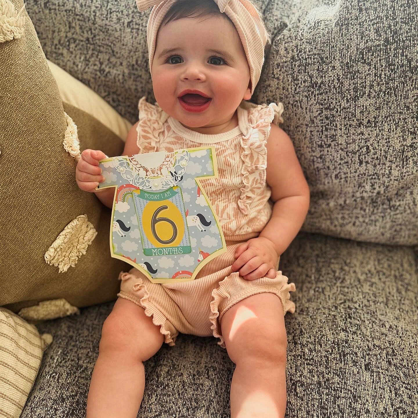 Mackenzie is registered to the contest to win money with this photo: baby, babylaughing, clothing, couch, cushion, face, furniture, happy, hat, head, homedecor, pants, person, photography, pillow, portrait, quilt, sitting, smile, t_shirt