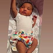 Ivie joined the competition — help win amazing prizes! baby, infant, child, onesie, skirt, floral_pattern, blanket, lying_down, arm_raised, cute, newborn, face, head, skin, person, indoors, soft_lighting, pattern, colorful, clothing