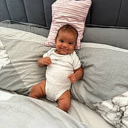 Shyro is registered to the contest to win money with this photo: baby, infant, smile, onesie, bed, pillow, striped_pillow, gray_bedding, marble_pattern, headboard, cute, child, happy, indoors, portrait, relaxed, young, person, resting, cozy