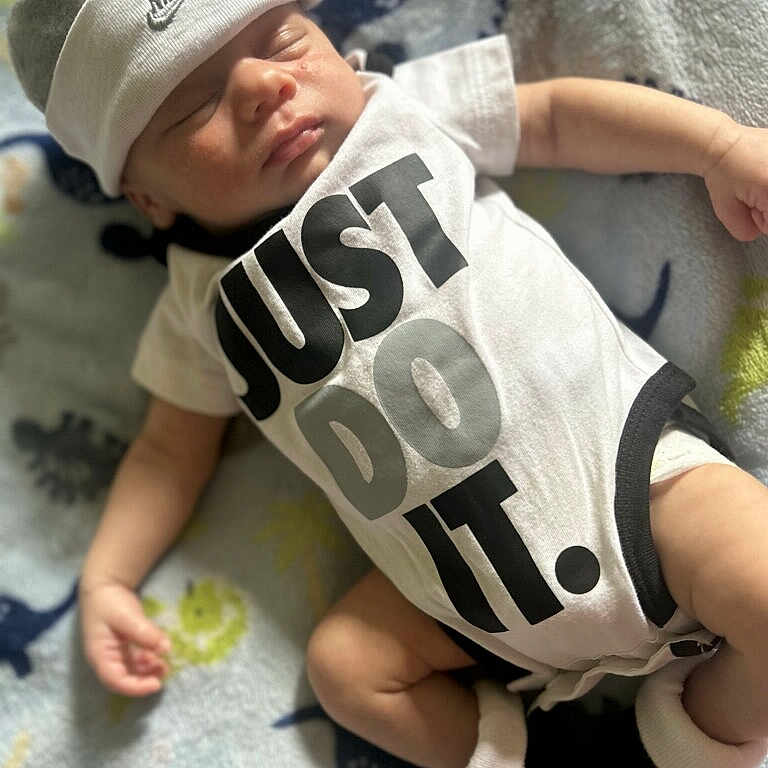 Lah'Moxi is registered to the contest to win money with this photo: baby, sleeping, infant, onesie, nike, hat, clothing, blanket, pattern, dinosaur, footwear, booties, child, cute, soft, peaceful, indoors, portrait, resting, newborn