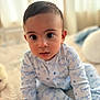 baby, child, pajamas, blue_text, mummy's_boy, sitting, bed, blanket, indoors, curious_eyes, face, person, cute, soft_light, close_up, young_child, infant, portrait, cozy, expression