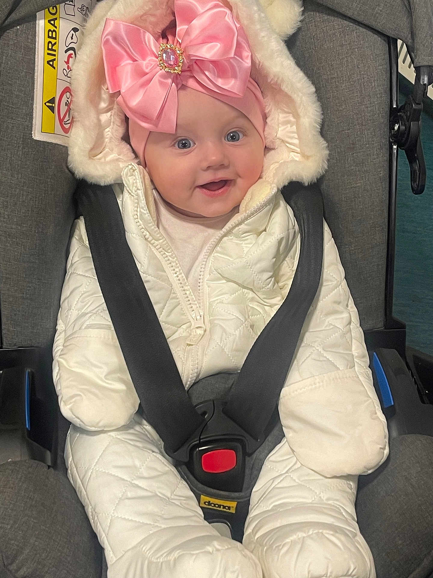 Zenayda joined the competition — help win amazing prizes! baby, child, car_seat, pink_bow, snowsuit, winter_clothing, smile, blue_eyes, face, seatbelt, infant, cute, warm, indoor, happy, headwear, padded_clothing, jacket, transport, safety