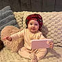 baby, child, headscarf, pink_pajamas, phone_case, couch, cushion, plush_texture, smile, sitting, indoor, face, person, cozy, soft_lighting, home, infant, cute, happy, portrait