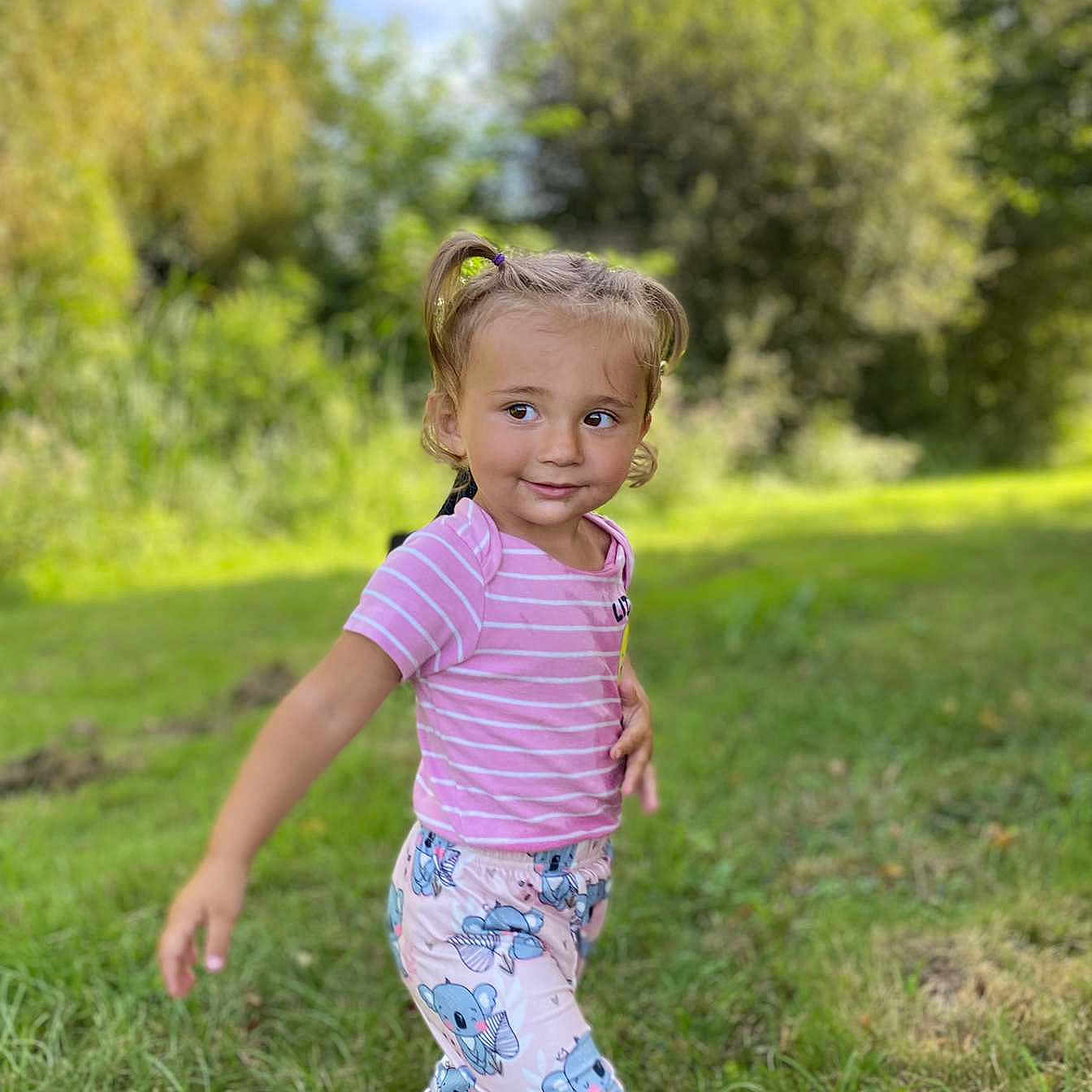 Sonaly a rejoint le concours — aidez-le/la à gagner de superbes lots ! casual_clothing, child, cute, daylight, grass, greenery, happy, koala_pants, nature, outdoor, person, pigtails, pink_shirt, playful, portrait, smile, sunlight, toddler, walking, young