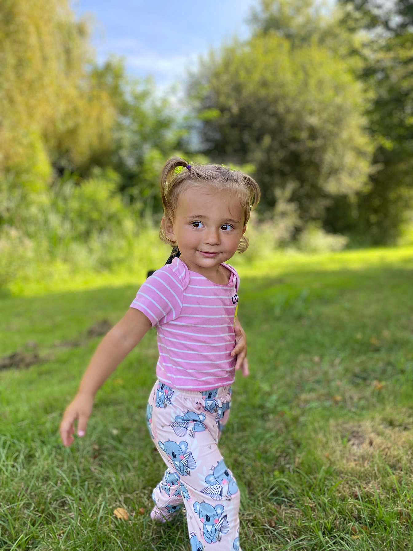 Sonaly a rejoint le concours — aidez-le/la à gagner de superbes lots ! child, toddler, grass, outdoor, nature, smile, pigtails, pink_shirt, koala_pants, playful, greenery, sunlight, young, person, cute, walking, casual_clothing, happy, daylight, portrait
