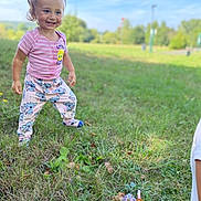 Sonaly a rejoint le concours — aidez-le/la à gagner de superbes lots ! toddler, child, smiling, outdoor, grass, field, pants, shirt, ponytail, happy, nature, daylight, playful, person, young_child, casual_clothing, greenery, blue_sky, sunny, park