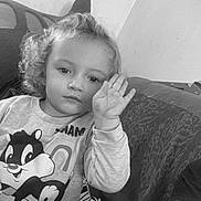 Solyna a rejoint le concours — aidez-le/la à gagner de superbes lots ! black_and_white, cartoon_shirt, casual_clothing, child, couch, curly_hair, cute, expression, face, hand, home, indoor, patterned_fabric, person, portrait, raising_hand, relaxed, sitting, young, young_child