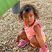 Melina joined the competition — help win amazing prizes! child, toddler, curious, outdoor, playground, wood_chips, pink_shoes, pink_top, orange_shorts, squatting, pointing, hair, expression, person, casual_clothing, daylight, play_area, green_structure, skin, face