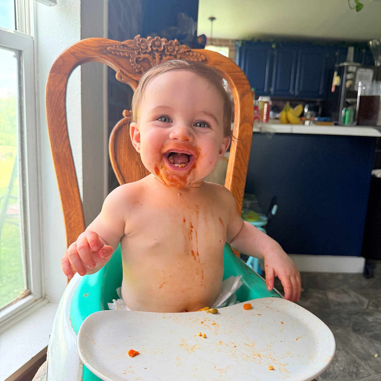 Rylee is registered to the contest to win money with this photo: baby, blue_cabinet, child, cute, face, floor, food, happy, high_chair, indoor, kitchen, light, messy, natural_light, person, plate, smiling, toddler, window, wooden_chair