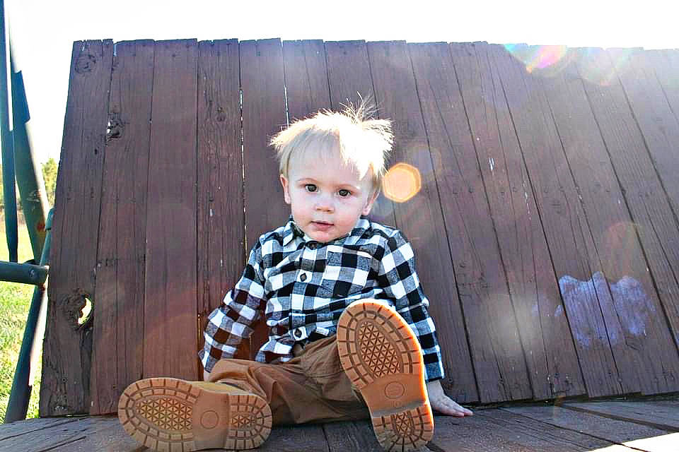 Grayson is registered to the contest to win money with this photo: ball, boot, chair, child, denim, flooring, grass, happy, knee, leisure, pattern, person, plaid, sitting, sleeve, sports_equipment, standing, tartan, tints_and_shades, toddler