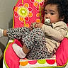 baby_chair, child, clothing, colorful, comfort, cozy, curly_hair, cute, expression, flower_pattern, indoor, infant, leopard_print, pacifier, pink, relaxed, sitting, toddler, white_sock, young_child