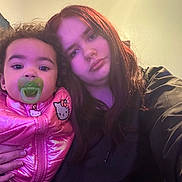 Shaniya joined the competition — help win amazing prizes! baby, child, pacifier, pink_jacket, hello_kitty, woman, long_hair, indoor, selfie, portrait, casual_clothing, curly_hair, neutral_expression, closeup, two_people, light_effect, purple_light, human, face, person