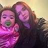 baby, child, pacifier, pink_jacket, hello_kitty, woman, long_hair, indoor, selfie, portrait, casual_clothing, curly_hair, neutral_expression, closeup, two_people, light_effect, purple_light, human, face, person