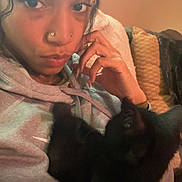 Astro joined the competition — help win amazing prizes! person, cat, indoor, hoodie, piercing, black_cat, couch, pillow, hand, face, fur, pet, relaxing, portrait, casual, cozy, furniture, looking, young_adult, expression