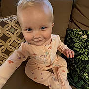 Lyla is registered to the contest to win money with this photo: baby, child, infant, couch, cushion, blue_eyes, blonde_hair, onesie, sitting, indoor, pattern, plush, smile, curious, hand, footed_pajamas, comfort, home, portrait, young