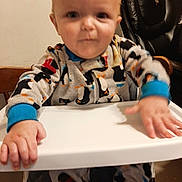 Jace joined the competition — help win amazing prizes! baby, child, high_chair, pajamas, indoor, furniture, face, hand, table, clothing, person, seat, wooden_chair, wall, floor, black_chair, cute, infant, home, blur