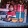 toddler, child, toy_train, wooden_toy, christmas_presents, gift_boxes, christmas_tree, holiday, red_sweater, floor, indoor, smiling, happy, festive, decorations, play, cute, portrait, sitting, holiday_season