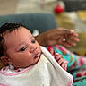 baby, infant, close_up, bib, pink_trim, curly_hair, hand, adult_hand, indoor, soft_focus, colorful_background, person, cute, newborn, portrait, tender_moment, skin, clothing, sleepwear, expression