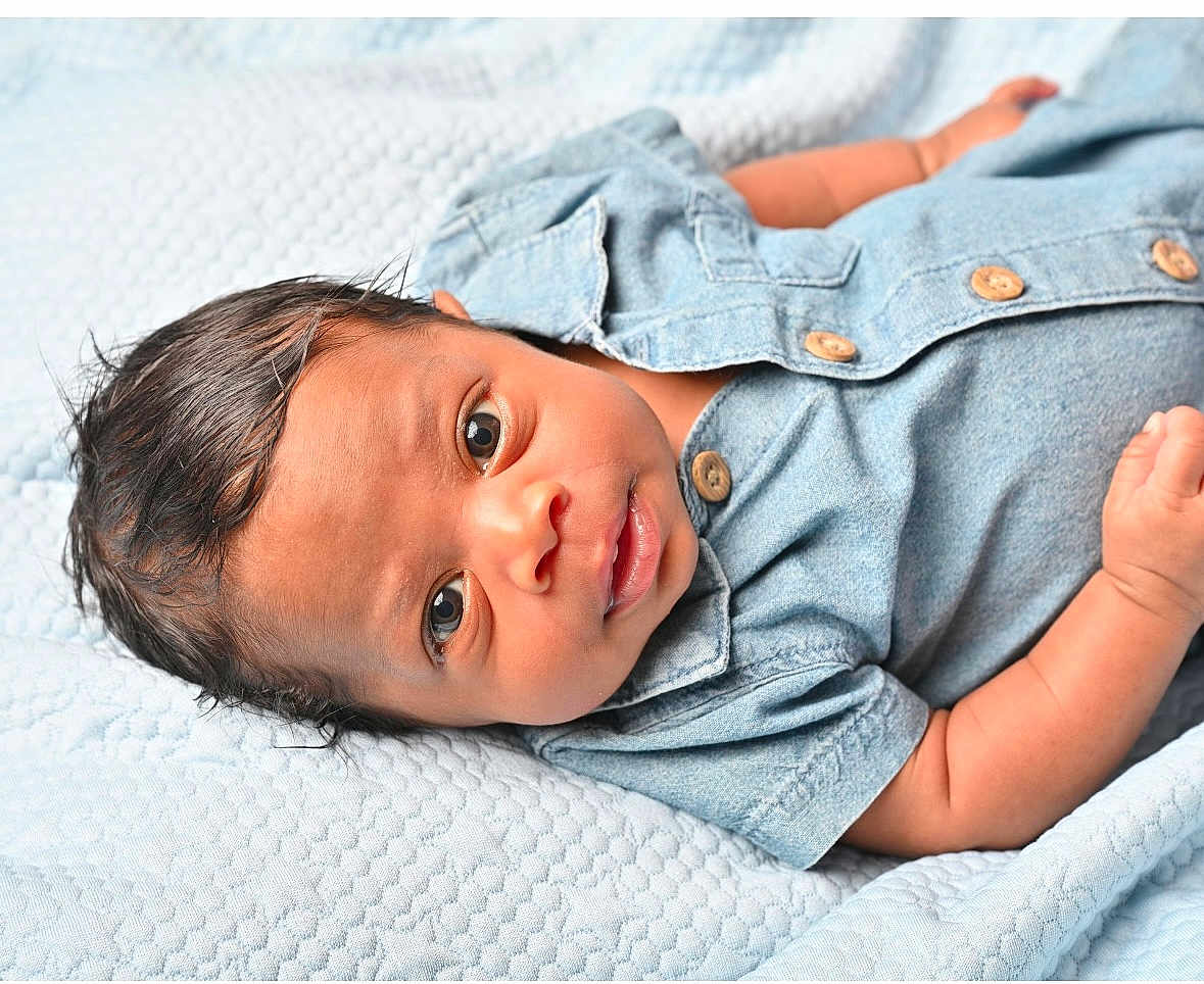 Jaxon is registered to the contest to win money with this photo: baby, infant, child, denim_shirt, blue_blanket, cute, portrait, lying_down, skin, face, eyes, hand, clothing, newborn, soft_texture, button, person, closeup, indoors, expression