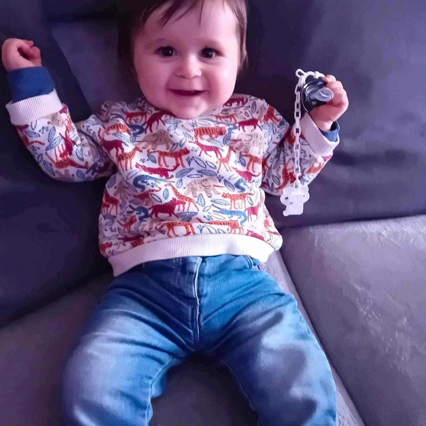 Këlyo participe au concours pour gagner de l'argent avec cette photo : ammunition, baby, bodypart, clothing, couch, face, finger, furniture, grenade, happy, head, jeans, pants, person, photography, portrait, sitting, sleeve, smile, weapon