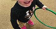 Navaya is registered to the contest to win money with this photo: animal_print_pants, black_shirt, carpet, casual_clothing, child, face, feet, girl, green_hoop, hair, happy, indoor, looking_up, person, photography, pink_shoes, playful, smiling, standing, toy