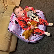 Navaya is registered to the contest to win money with this photo: toddler, child, pacifier, plush_toy, stuffed_animal, bean_bag, doll, onesie, red_clothing, black_clothing, carpet, sofa, indoor, floor_tiles, toy, cute, baby, sitting, playtime, home