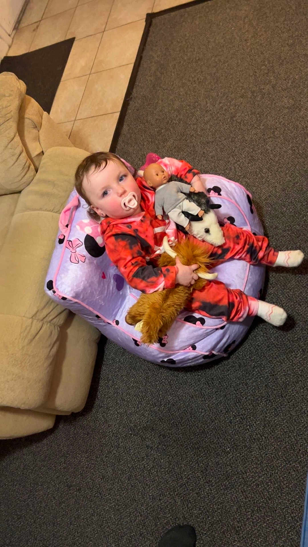 Navaya is registered to the contest to win money with this photo: toddler, child, pacifier, plush_toy, stuffed_animal, bean_bag, doll, onesie, red_clothing, black_clothing, carpet, sofa, indoor, floor_tiles, toy, cute, baby, sitting, playtime, home
