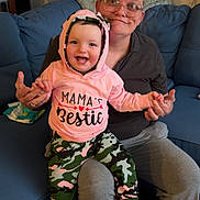 Navaya is registered to the contest to win money with this photo: baby, child, woman, glasses, hoodie, pink_clothing, camo_pants, socks, couch, living_room, smiling, happy, indoor, person, holding_hands, seated, casual_clothing, home, family, portrait