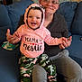 baby, child, woman, glasses, hoodie, pink_clothing, camo_pants, socks, couch, living_room, smiling, happy, indoor, person, holding_hands, seated, casual_clothing, home, family, portrait