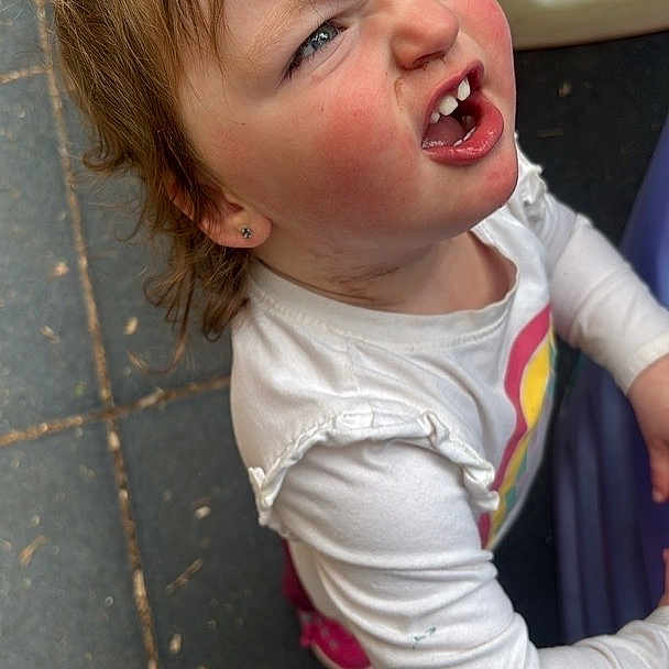 Navaya is registered to the contest to win money with this photo: child, toddler, face, expression, white_shirt, rainbow_print, outdoor, playground, curly_hair, rosy_cheeks, looking_up, casual_clothing, standing, daylight, person, young_child, play_area, colorful, emotion, active