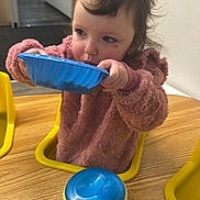 Navaya joined the competition — help win amazing prizes! toddler, child, indoor, table, sippy_cup, blue_bowl, pink_sweater, yellow_chair, wooden_table, face, hair, person, eating, drinking, baby, room, wall_art, playroom, furniture, curly_hair