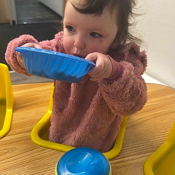 Navaya joined the competition — help win amazing prizes! toddler, child, indoor, table, sippy_cup, blue_bowl, pink_sweater, yellow_chair, wooden_table, face, hair, person, eating, drinking, baby, room, wall_art, playroom, furniture, curly_hair