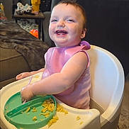Navaya joined the competition — help win amazing prizes! baby, high_chair, food, messy, pink_bib, smiling, indoor, living_room, child, person, table, plate, feeding_time, happy, couch, toy, home, meal, cute, toddler