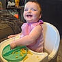 baby, high_chair, food, messy, pink_bib, smiling, indoor, living_room, child, person, table, plate, feeding_time, happy, couch, toy, home, meal, cute, toddler