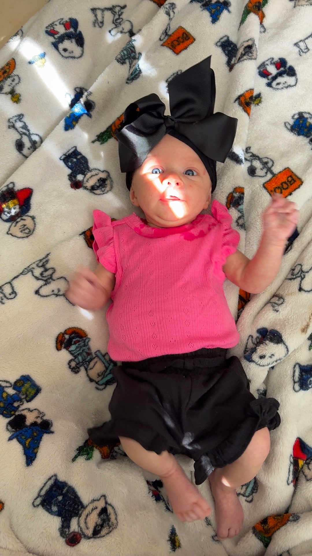 Kali joined the competition — help win amazing prizes! baby, infant, child, blanket, snoopy, headband, bow, pink_top, black_shorts, blue_eyes, sunlight, cute, laying_down, expression, arms, feet, patterned_blanket, soft_texture, indoors, colorful