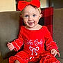 baby, child, smiling, red_outfit, headband, red_bow, sitting, chair, plaid_blanket, indoors, cute, happy, portrait, festive, holiday_theme, person, infant, clothing, face, hands