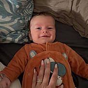 Elio a rejoint le concours — aidez-le/la à gagner de superbes lots ! baby, infant, smiling, orange_outfit, hand, tattoo, bed, pillow, blanket, manicure, person, face, lying_down, cozy, cute, child, indoor, soft_lighting, comfort, relaxed