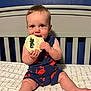 baby, infant, crib, mattress, wooden_sign, eight_months, blue_wall, navy_blue_outfit, red_crabs, chewing, sitting, cute, child, indoors, smiling, happy, face, hand, legs, milestone