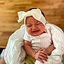 baby, infant, blanket, headband, white_clothing, cute, expression, hand, face, newborn, indoors, skin, person, soft_texture, wrapped, child, small, comfort, wooden_background, sitting